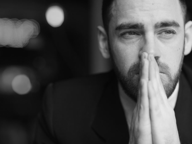 Portrait of modern bearded businessman looking away with red teary eyes, stressed and tired against black background, covering his mouth with hands