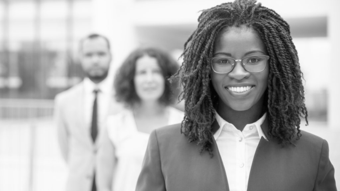 Cheerful young African American businesswoman. Portrait of confident female boss smiling at camera while standing with multiethnic colleagues, selective focus. Leadership concept