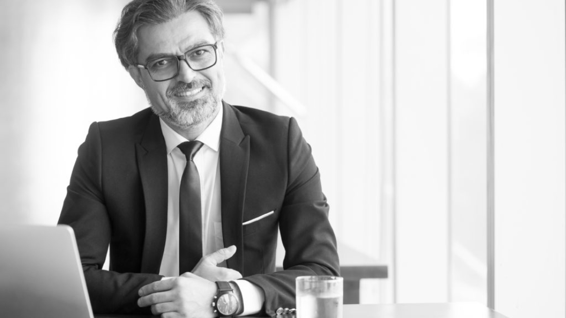 Cheerful businessman in eyeglasses working in office or coworking space. Portrait of confident male executive with gray hair at table. Successful business concept
