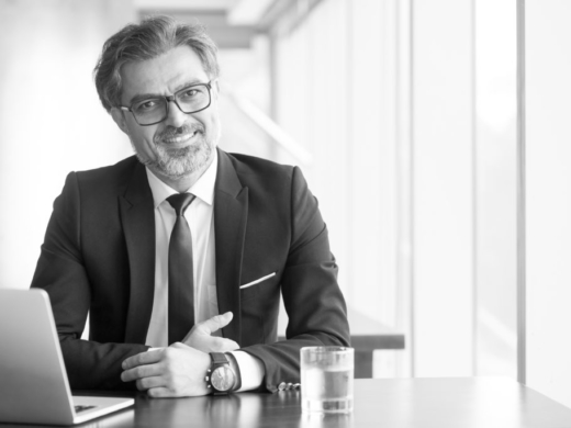 Cheerful businessman in eyeglasses working in office or coworking space. Portrait of confident male executive with gray hair at table. Successful business concept
