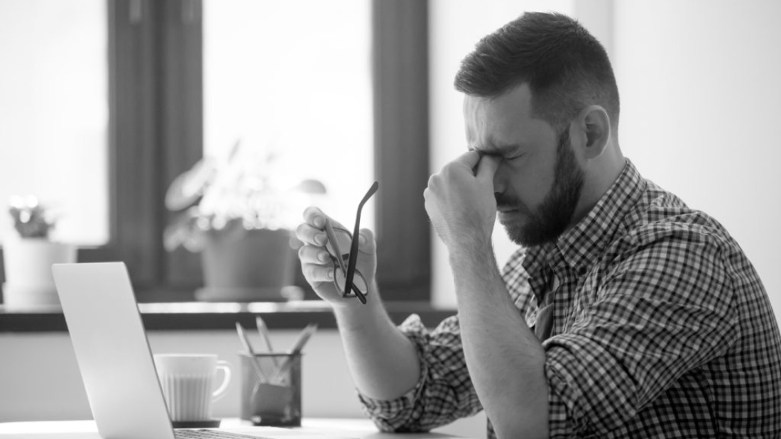 Tired stressed male worker taking off glasses, person massaging nose bridge suffering from headache and trying to relieve pain. Despaired man frustrated after reading company collapse or failure news
