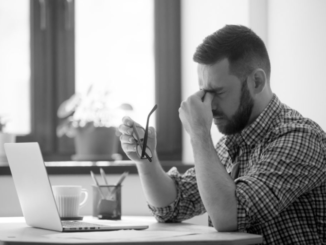 Tired stressed male worker taking off glasses, person massaging nose bridge suffering from headache and trying to relieve pain. Despaired man frustrated after reading company collapse or failure news